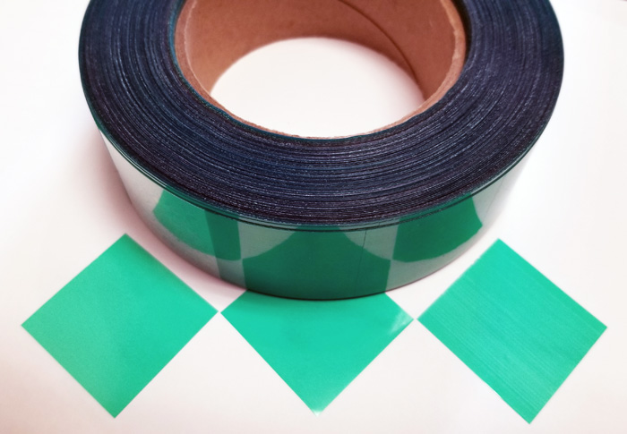 Green polyester die cut tape squares on a roll